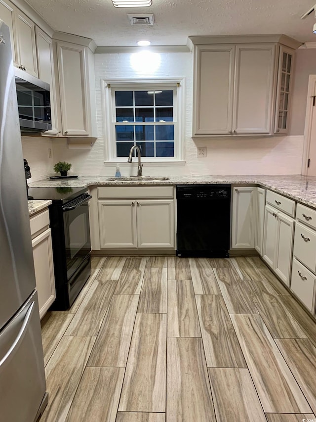 kitchen featuring light stone countertops, wood tiled floor, a textured ceiling, black appliances, and a sink