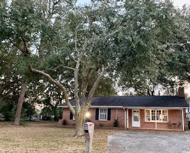 ranch-style home with driveway, a chimney, and brick siding