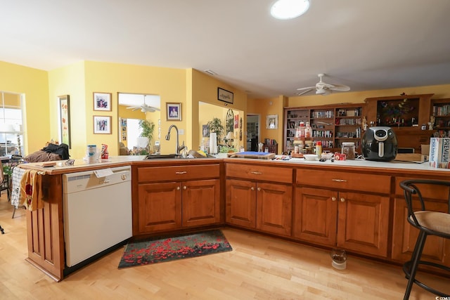 kitchen with a sink, a ceiling fan, light wood-style floors, brown cabinets, and dishwasher