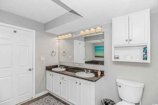 full bathroom featuring double vanity, a textured ceiling, toilet, and a sink