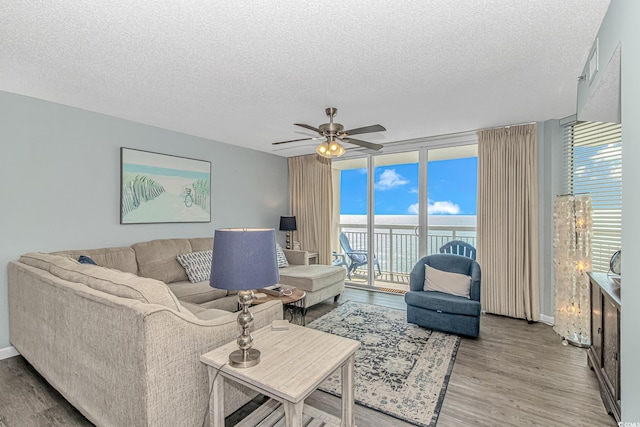 living room featuring a water view, light wood-type flooring, a textured ceiling, ceiling fan, and baseboards