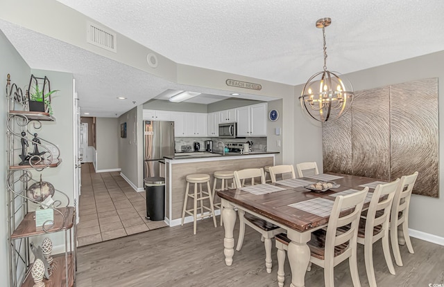dining room with baseboards, a notable chandelier, light wood-style flooring, and visible vents