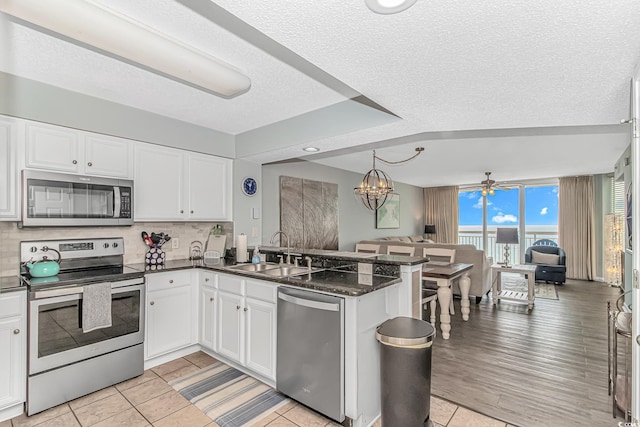 kitchen with a sink, white cabinetry, a peninsula, open floor plan, and stainless steel appliances