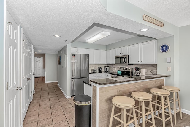 kitchen with a peninsula, a sink, a textured ceiling, appliances with stainless steel finishes, and decorative backsplash
