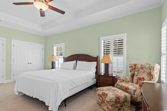 carpeted bedroom with a tray ceiling, multiple windows, and crown molding