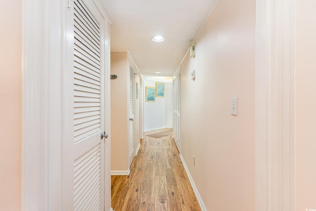 hall featuring light wood finished floors, baseboards, a textured ceiling, and recessed lighting