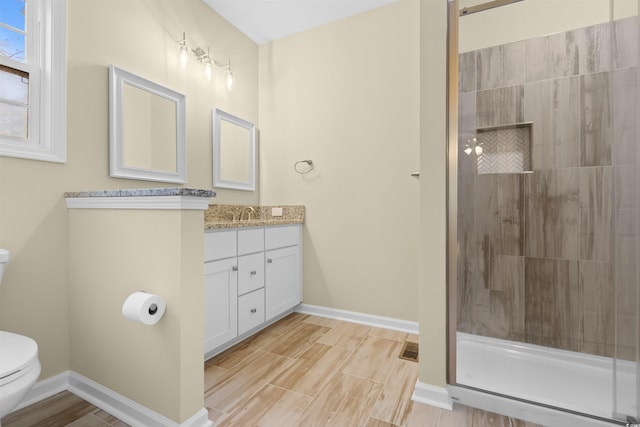 bathroom with toilet, wood tiled floor, a tile shower, vanity, and baseboards