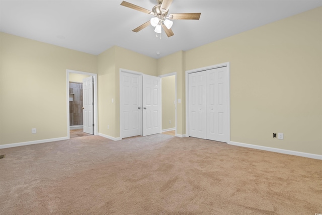 unfurnished bedroom with carpet, multiple closets, ensuite bathroom, a ceiling fan, and baseboards