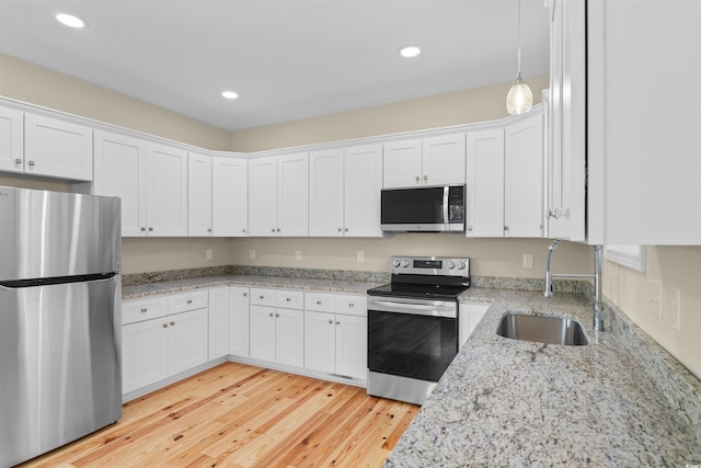 kitchen featuring appliances with stainless steel finishes, a sink, light wood-style floors, and white cabinets