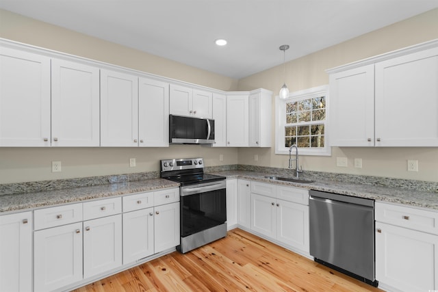 kitchen with light wood finished floors, decorative light fixtures, stainless steel appliances, white cabinetry, and a sink