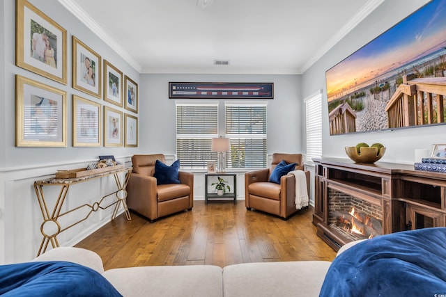 sitting room featuring a warm lit fireplace, hardwood / wood-style floors, visible vents, and crown molding