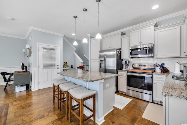 kitchen with stainless steel appliances, a kitchen breakfast bar, a center island, dark wood finished floors, and crown molding