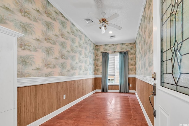 empty room featuring a wainscoted wall, wallpapered walls, crown molding, and visible vents