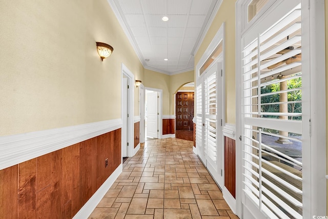 hallway with arched walkways, a wainscoted wall, stone finish floor, and a wealth of natural light