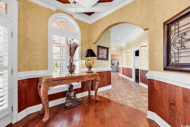 corridor with arched walkways, wainscoting, crown molding, and hardwood / wood-style flooring