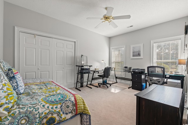 bedroom with a textured ceiling, light colored carpet, a ceiling fan, visible vents, and a closet