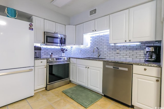 kitchen featuring visible vents, dark stone counters, stainless steel appliances, white cabinetry, and a sink