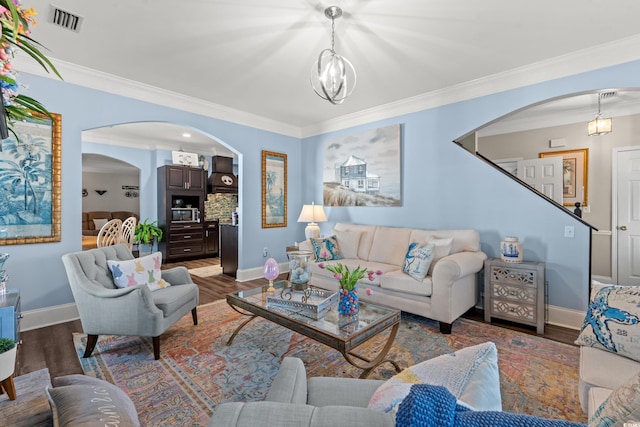 living area featuring arched walkways, wood finished floors, visible vents, ornamental molding, and an inviting chandelier