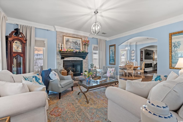 living area featuring arched walkways, wood finished floors, an inviting chandelier, crown molding, and a stone fireplace