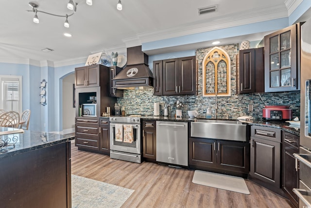 kitchen featuring arched walkways, light wood-style flooring, stainless steel appliances, premium range hood, and visible vents