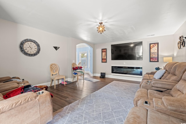 living room featuring arched walkways, visible vents, a glass covered fireplace, wood finished floors, and baseboards