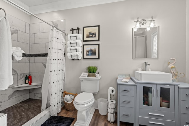 bathroom featuring crown molding, toilet, vanity, wood finished floors, and tiled shower