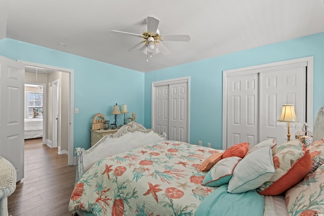 bedroom with attic access, baseboards, a ceiling fan, wood finished floors, and two closets