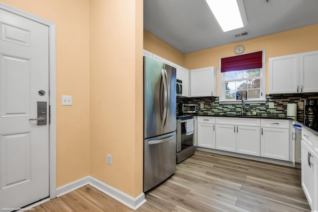 kitchen featuring visible vents, a sink, stainless steel appliances, white cabinetry, and backsplash