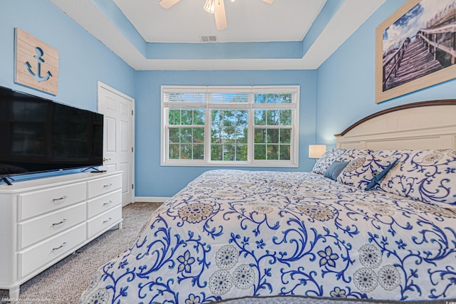 carpeted bedroom with baseboards, visible vents, a raised ceiling, and a ceiling fan