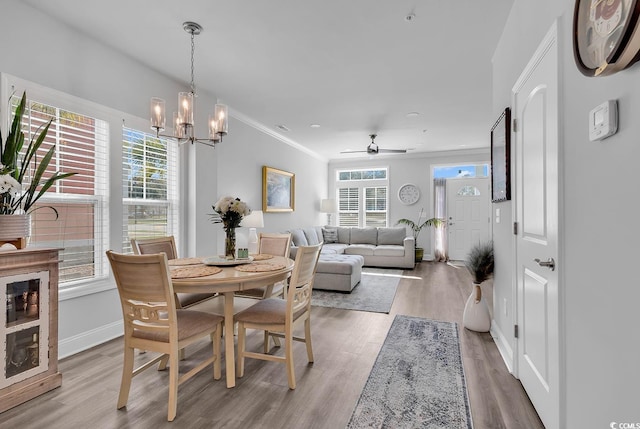 dining space featuring light wood-style floors, ornamental molding, baseboards, and ceiling fan with notable chandelier