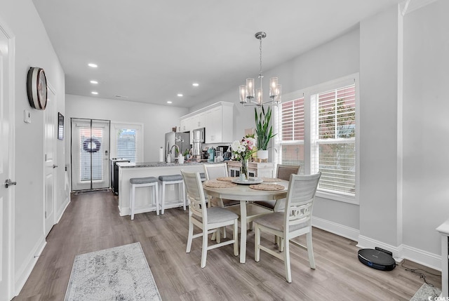 dining space featuring baseboards, light wood-style flooring, a wealth of natural light, and an inviting chandelier