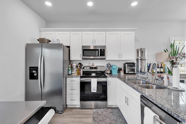 kitchen featuring stainless steel appliances, white cabinetry, a sink, dark stone countertops, and light wood-type flooring