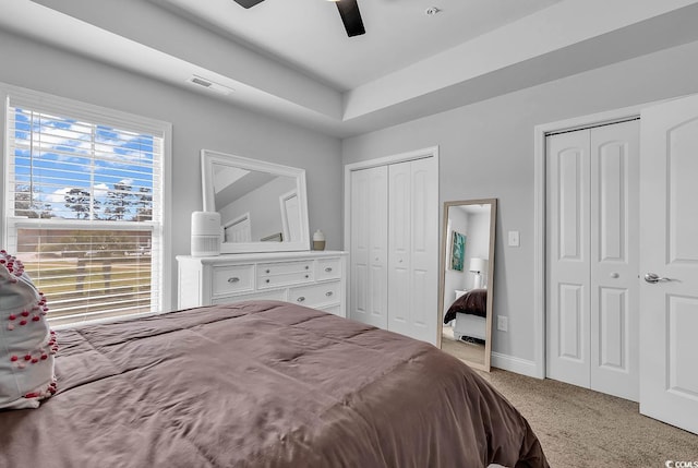 carpeted bedroom with a ceiling fan, two closets, visible vents, and baseboards