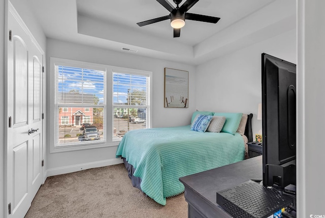 bedroom featuring light carpet, baseboards, visible vents, a raised ceiling, and ceiling fan