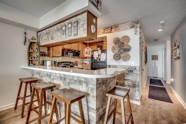 bar with a textured ceiling, baseboards, decorative backsplash, black appliances, and light wood finished floors