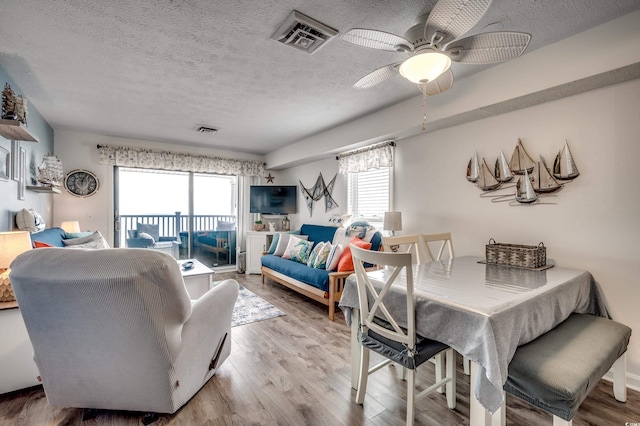 dining room featuring a textured ceiling, ceiling fan, wood finished floors, and visible vents