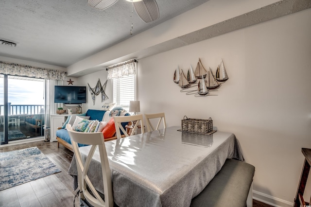 dining area featuring visible vents, a ceiling fan, a textured ceiling, wood finished floors, and baseboards