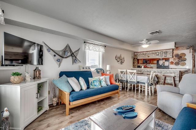 living area with a ceiling fan, a textured ceiling, visible vents, and wood finished floors