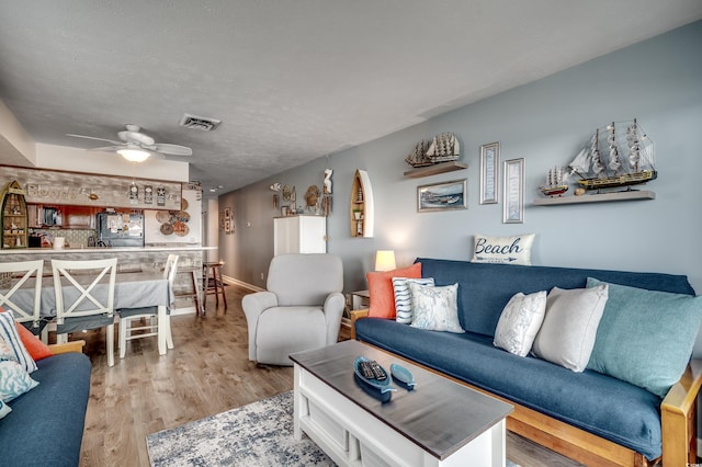 living area with baseboards, visible vents, ceiling fan, wood finished floors, and a textured ceiling