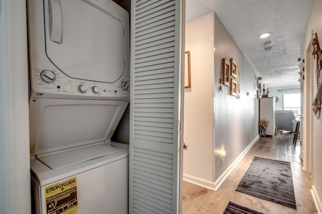 washroom featuring a textured ceiling, laundry area, wood finished floors, baseboards, and stacked washer and clothes dryer