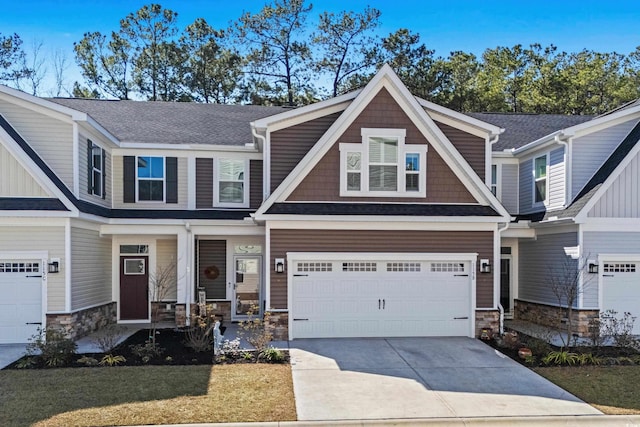 view of front of property featuring stone siding, roof with shingles, driveway, and an attached garage