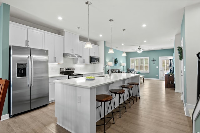 kitchen featuring a breakfast bar area, appliances with stainless steel finishes, a sink, under cabinet range hood, and backsplash