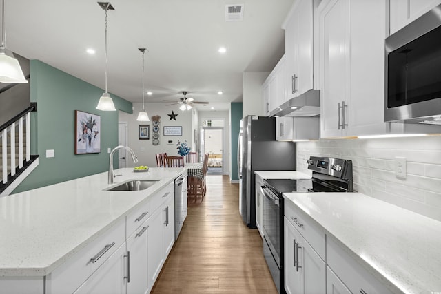 kitchen featuring under cabinet range hood, stainless steel appliances, a sink, visible vents, and decorative backsplash