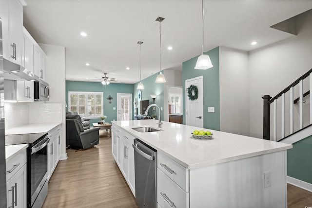 kitchen with decorative backsplash, light wood-style flooring, appliances with stainless steel finishes, open floor plan, and a sink