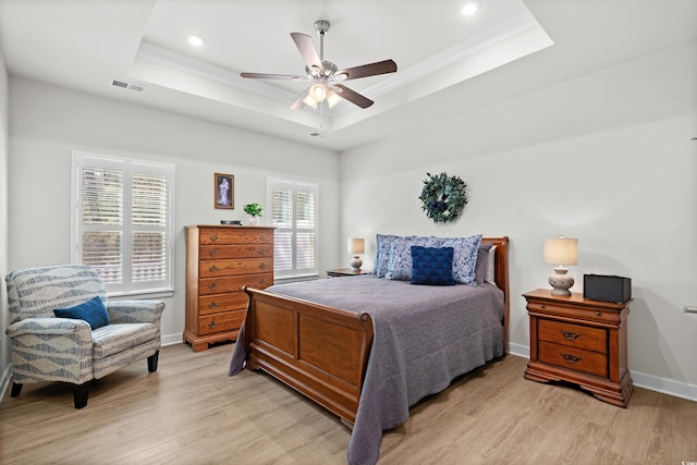 bedroom featuring light wood-style floors, a raised ceiling, and baseboards