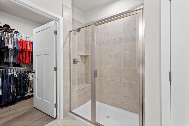 bathroom featuring a walk in closet, a shower stall, and wood finished floors