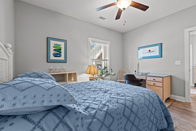 bedroom with a ceiling fan, visible vents, baseboards, and wood finished floors