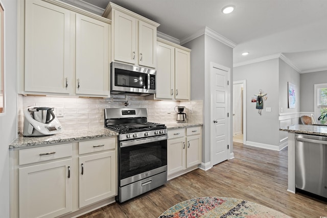 kitchen featuring baseboards, ornamental molding, appliances with stainless steel finishes, light wood-type flooring, and tasteful backsplash