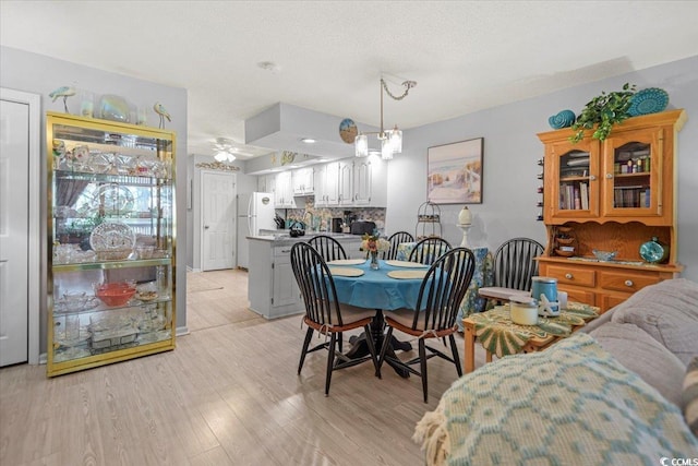 dining space featuring light wood-style flooring and ceiling fan with notable chandelier