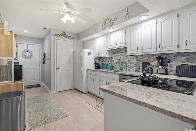 kitchen featuring a sink, freestanding refrigerator, white cabinetry, light wood-type flooring, and decorative backsplash